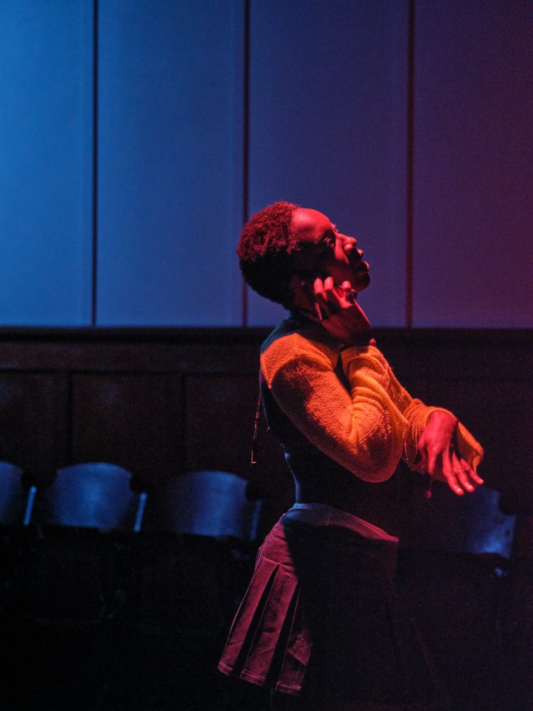 Samra gesticulates with her hands and she walks and talks on the phone bathed in pink light.