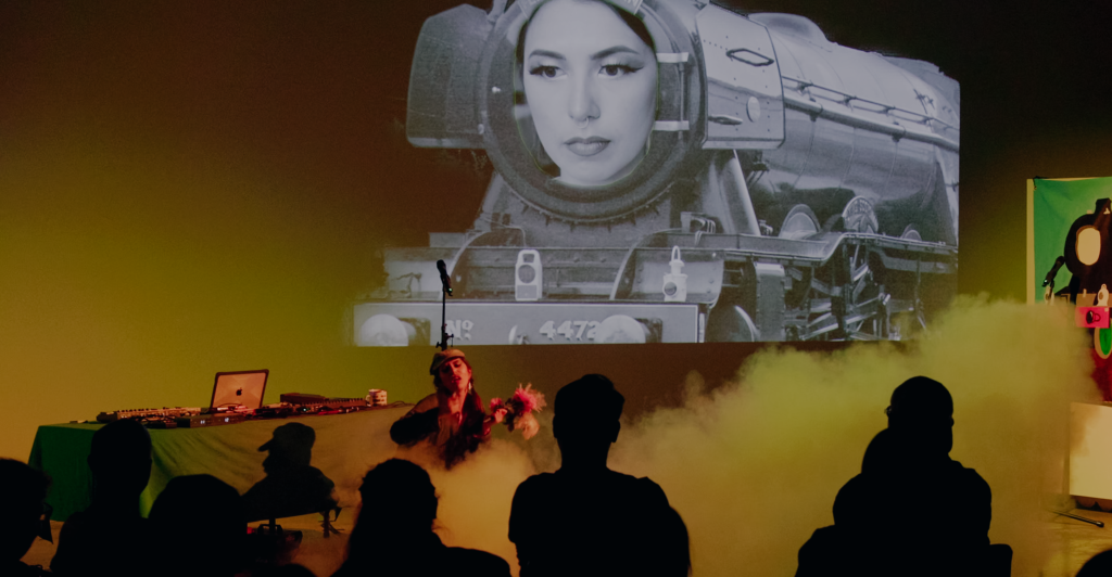 Megan dances through a cloud of smoke holding a bouquet of fake flowers. A black and white 4472 train engine with Megan's face on it is projected on the back wall.