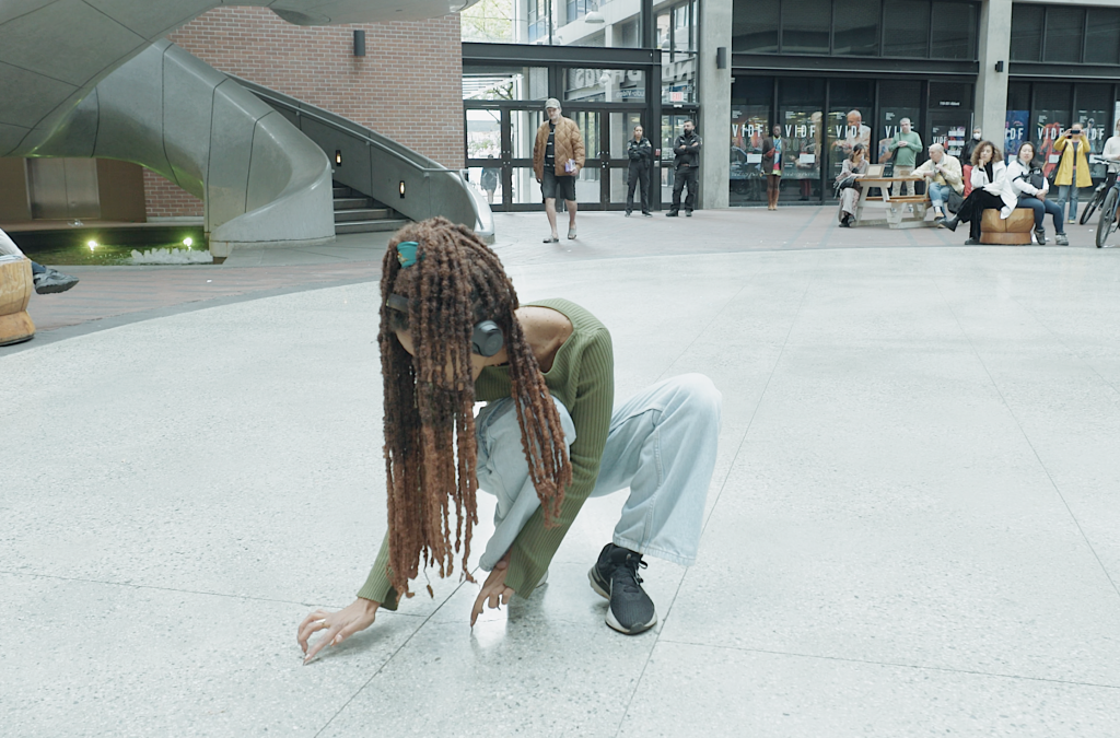 Jessica's dreadlocks encircle her body as she crouches down, tapping her acrylic nails on the concrete floor.