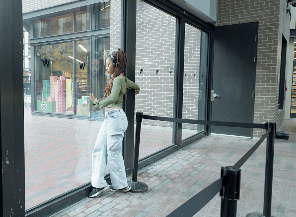 Jessica steps gently, one foot over the other, in front of a wall of windows.