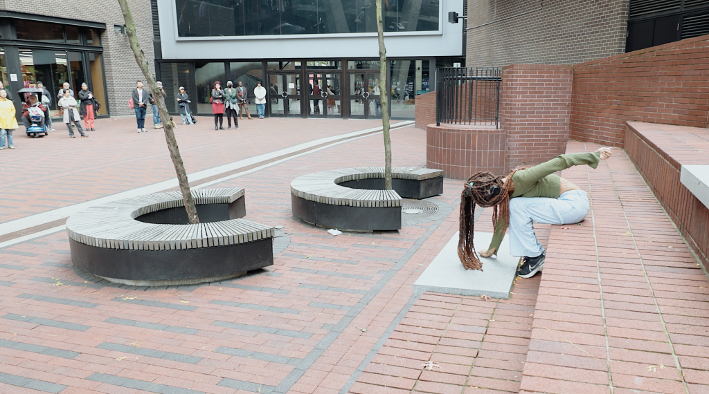 Jessica sits on a large brick stair, her dreadlocks brushing the floor as she leans forward stretching her arms in either direction like she's pulling an invisible rope. 
