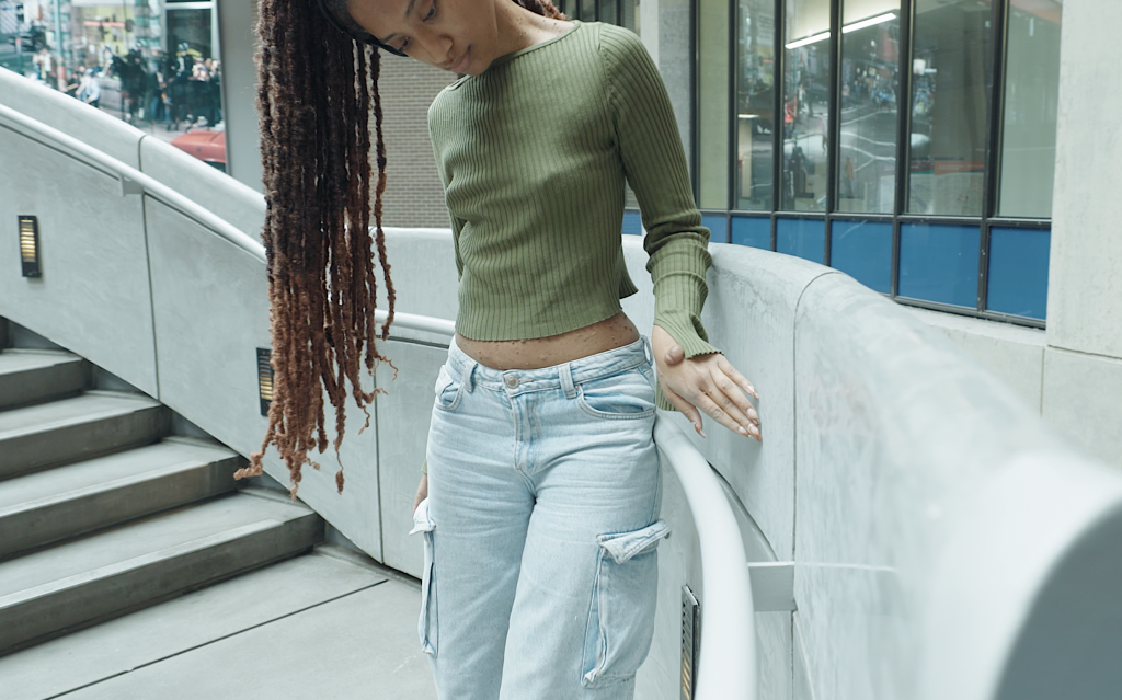 Jessica looks towards the ground as her hand runs along a low concrete wall next to the stairwell railing. 