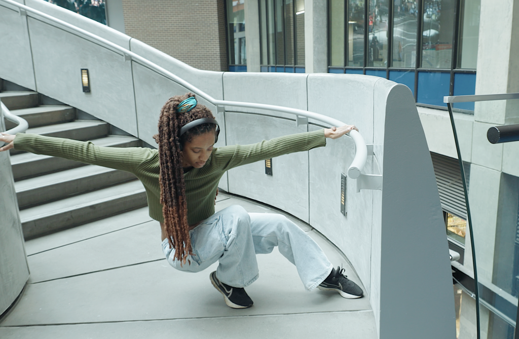 Jessica's long dreadlocks brush her hip as she squats down gracefully with arms stretched between the railings on either side of the concrete stairwell. 
