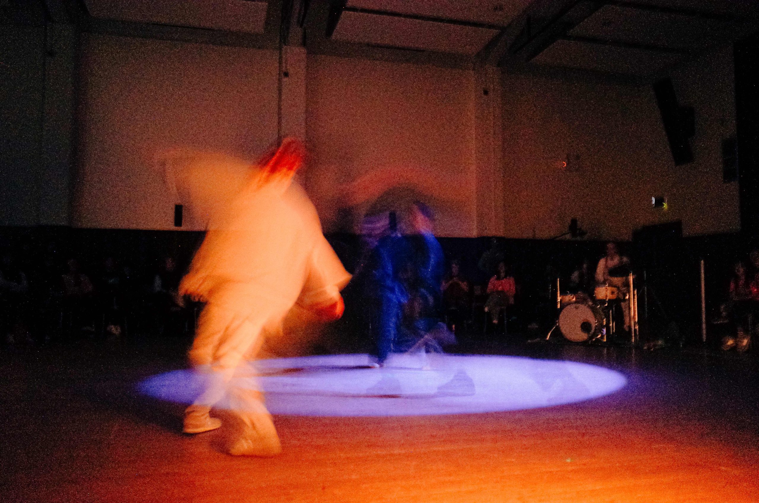 A drummer plays in the corner as dancers bodies blur in a sea of warm light. As they move through space their aura's time laps delay behind each motion as they circle a purple spotlight.