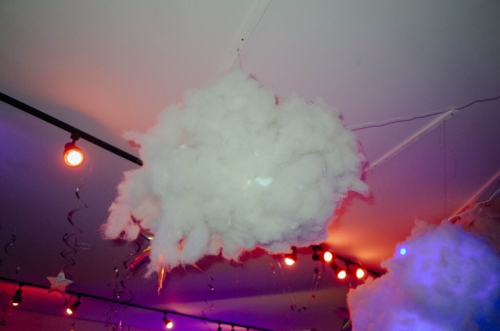A fluffy cotton-ball cloud dangles form the celling encircled in orange and pink lights and star streamers.